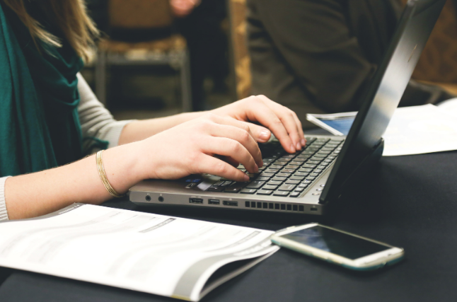 A woman sat at a desk typing on a laptop. The image is focussed on her hands.