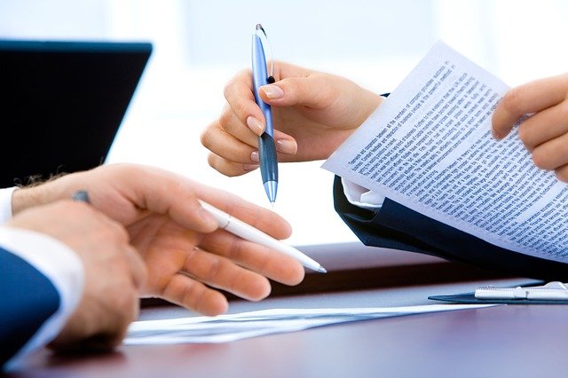 man and woman holding contracts sat at desk, focus on hands, faces out of shot