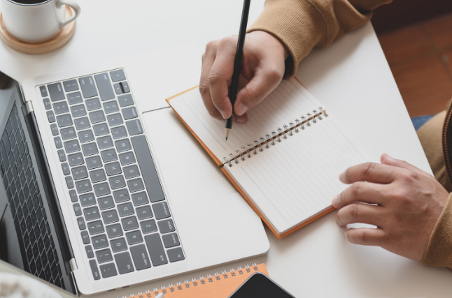 woman writing on a notepad in front of her laptop, taken from above