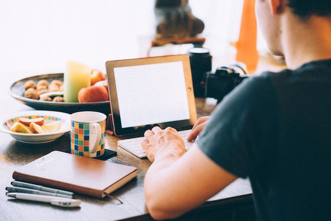 man writing on computer surround by supplies on desk