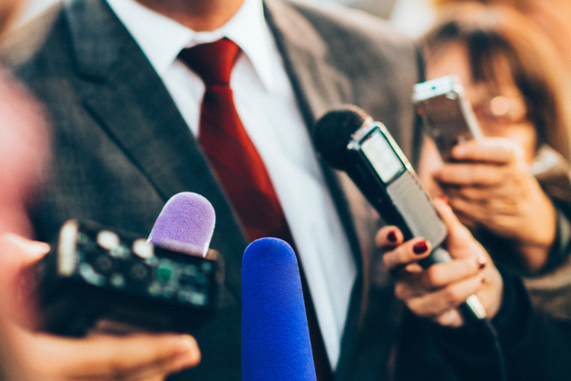 hands holding microphones up to man in suit