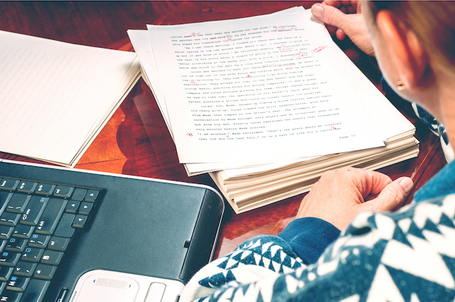 woman sat at laptop with proofread manuscript