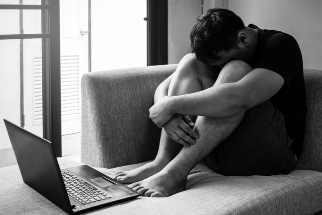 dejected man with head on knees in front of laptop on sofa