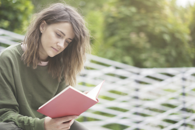 woman reading a red book while sat in a garden