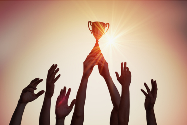 hands lifting trophy, silhouetted against a sunset