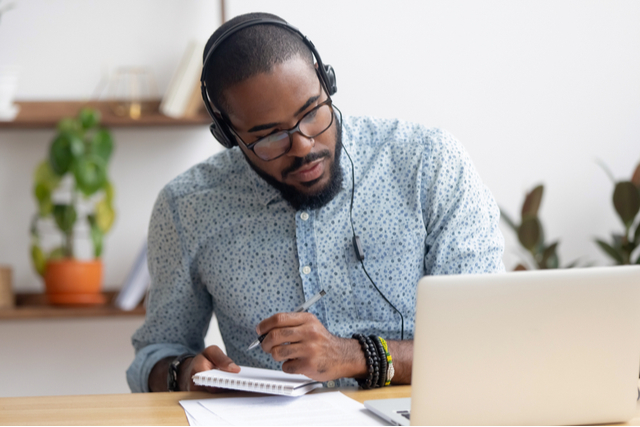 man focussing on notebook while listening to computer