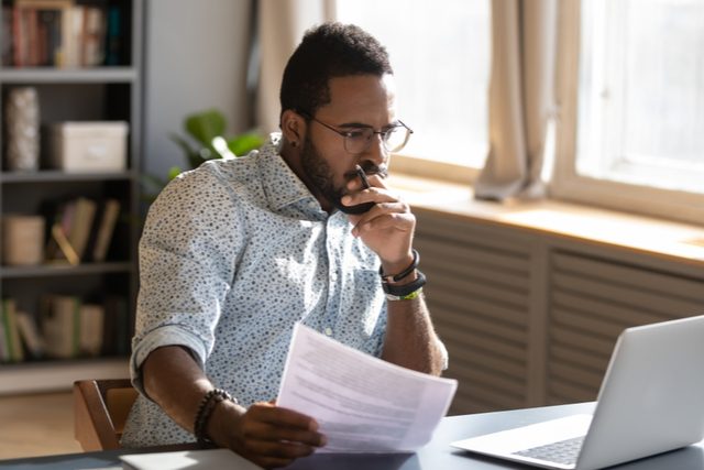 man holds pen and paper, looking at screen