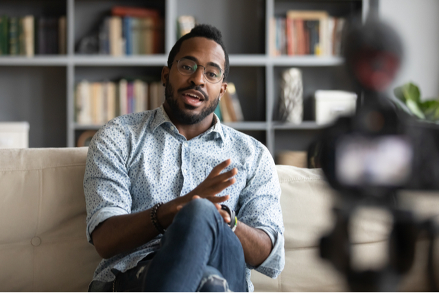 focus on man talking to a camera, which is out of focus in the foreground