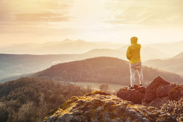 man looking out over a forest from a peak at sunrise