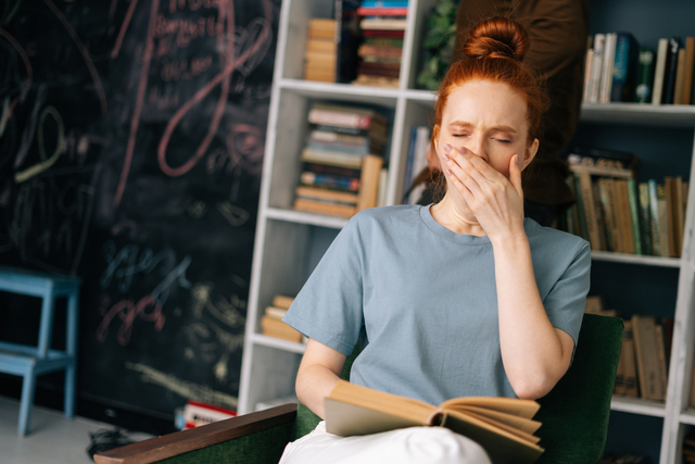 woman yawns while reading a book