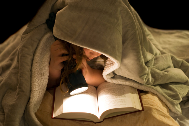 girl reading in bed with a tourch