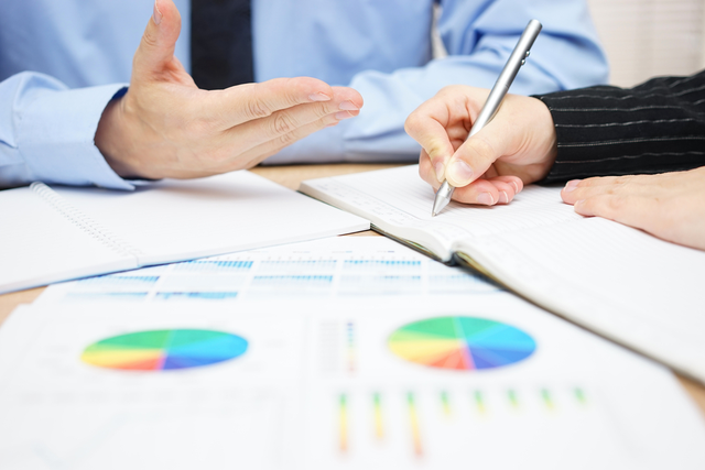 shot of business documents on a desk, with business peoples' hands pointing to areas of text