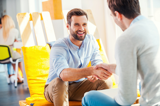 smiling man shakes hands with another man who has his back to the camera