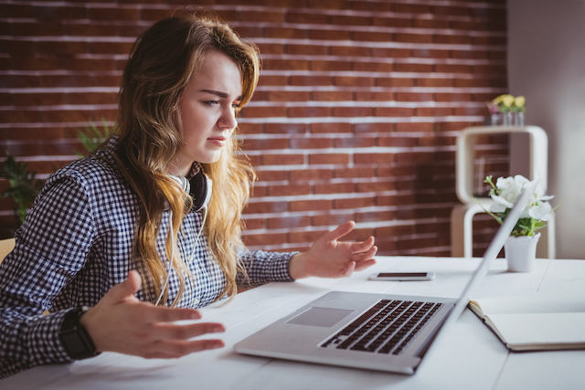 woman holds hands up in confusion while looking at laptop screen