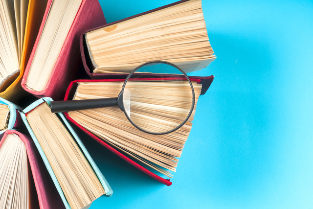 Top view of colorful hardback books in a circle and magnifying glass.