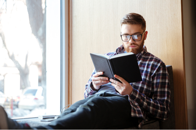 man reads book in windowsill