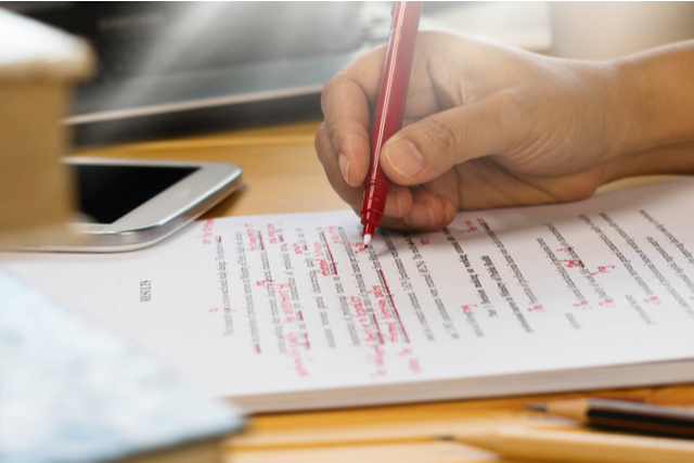 hand holding a pen over a manuscript marked in red