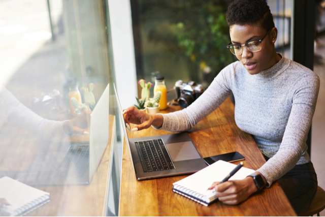 woman reading on laptop and making notes