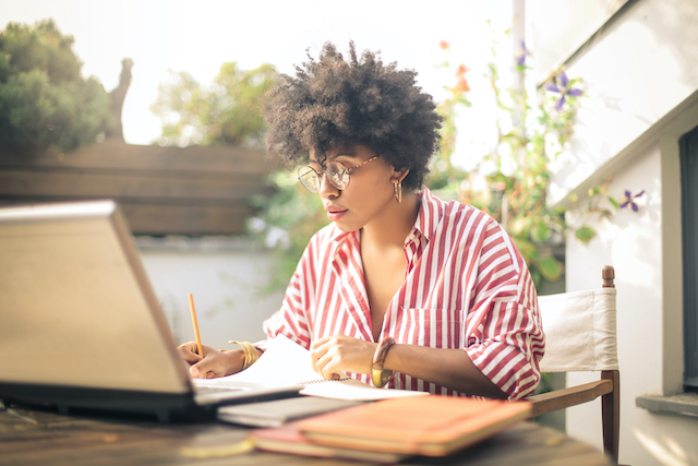 woman sat in front of laptop, writing on a piece of paper