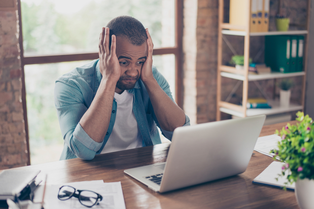 man holds his head in his hands, looking frustratedly at a screen