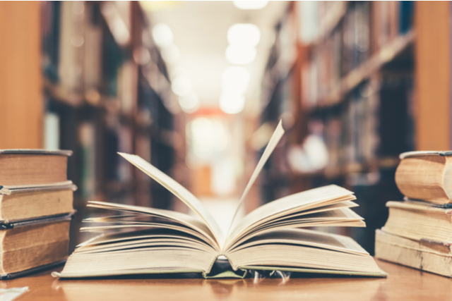 an open book on a desk, a library is out of focus in the background