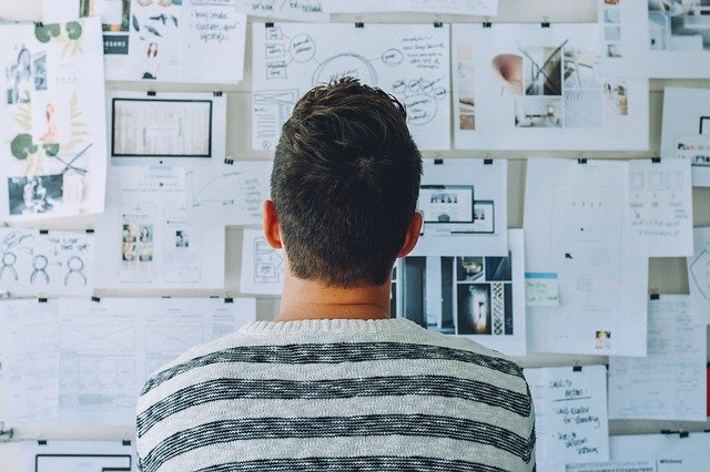 man looking at a wall covered in notes, plans and designed