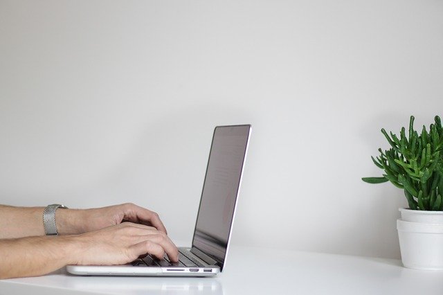 side view of a man's hands typing on a laptop