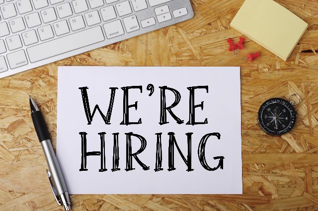 paper saying 'we're hiring' on a wooden desk